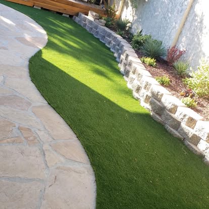 Flagstone walkway curving alongside artificial grass and a stacked block retaining wall