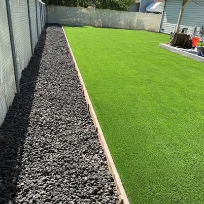 Narrow artificial grass lawn running beside a black rock drainage strip