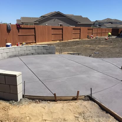 Poured patio slab meeting a new block retaining wall at the edge of a yard
