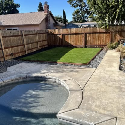 Concrete pool deck wrapping a backyard pool with an artificial grass panel alongside it