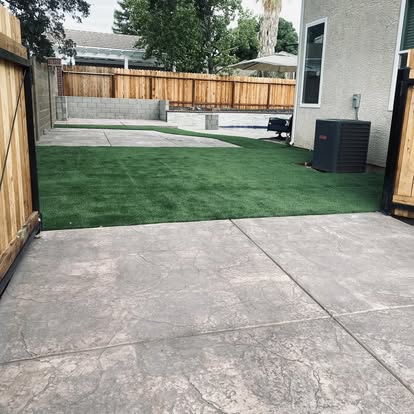 Stamped concrete patio wrapping an artificial grass lawn in a finished backyard