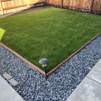 Artificial grass lawn squared off inside a cobble rock border in a low-maintenance backyard