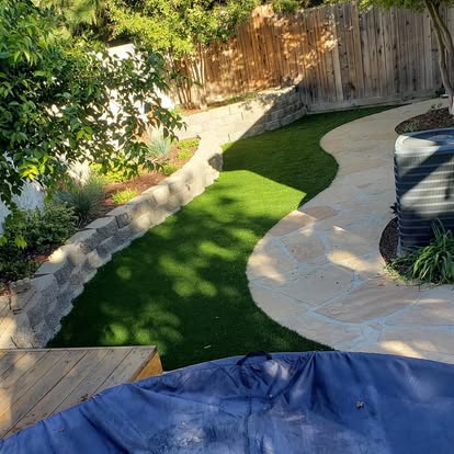 Retaining wall holding a planted slope above a turf lawn and stone path