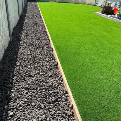 Artificial grass strip laid between a rock border and a concrete edge